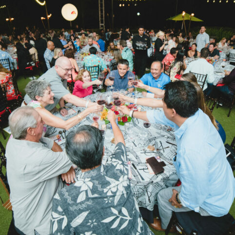 Guests at a seated dinner event toasting red wine at their table under the stars